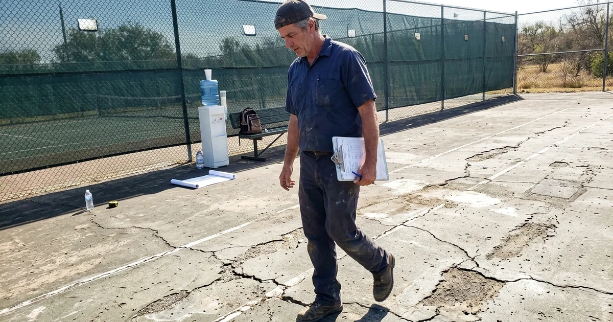 Builder assessing a worn court surface with a clipboard