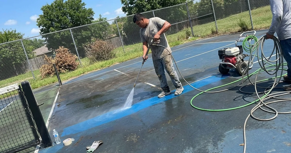 Crew pressure washing a sport court with a clean stripe emerging beside the dirty area