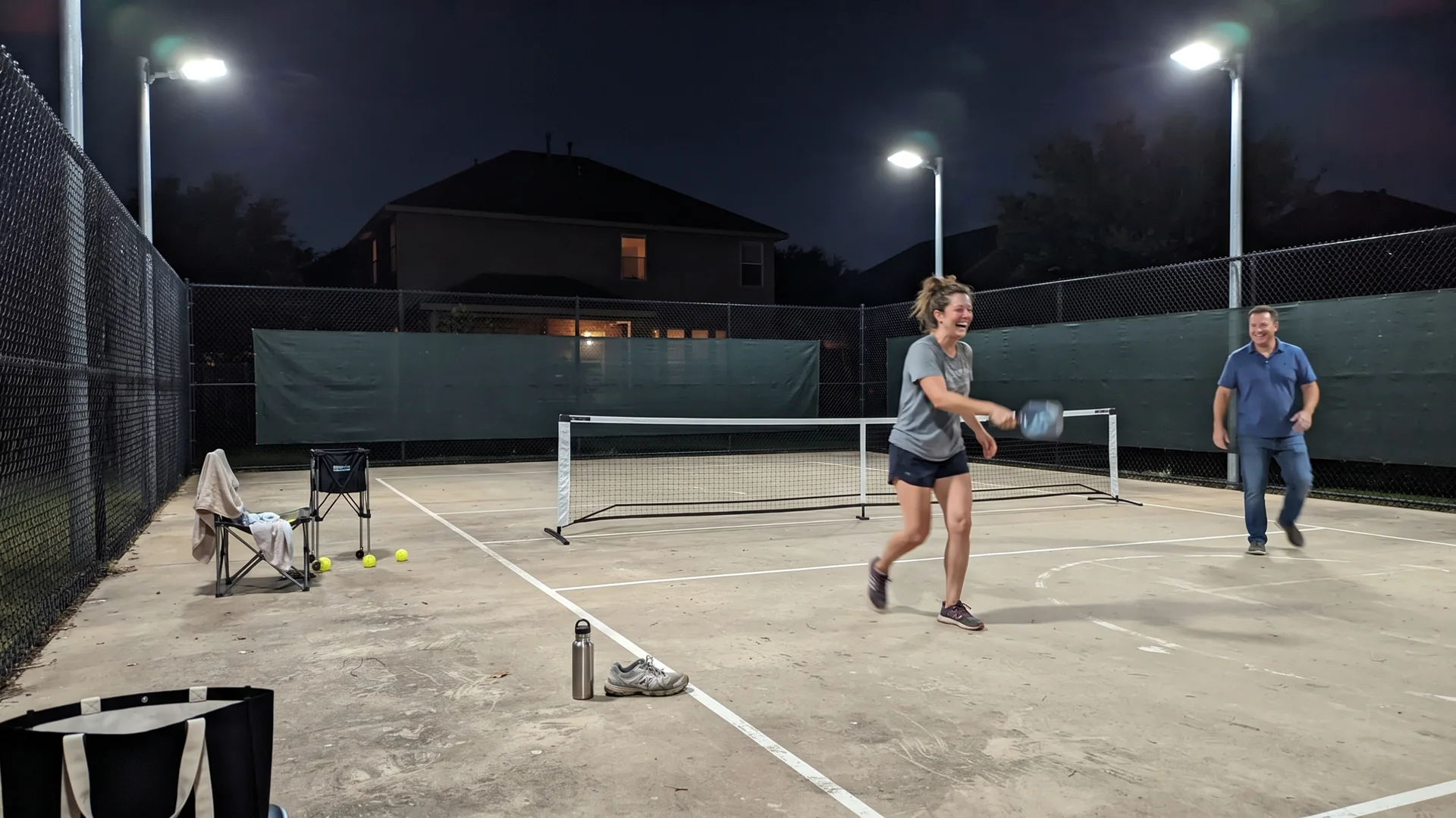 Backyard court lit at night by LED floodlights with perimeter fencing and windscreens