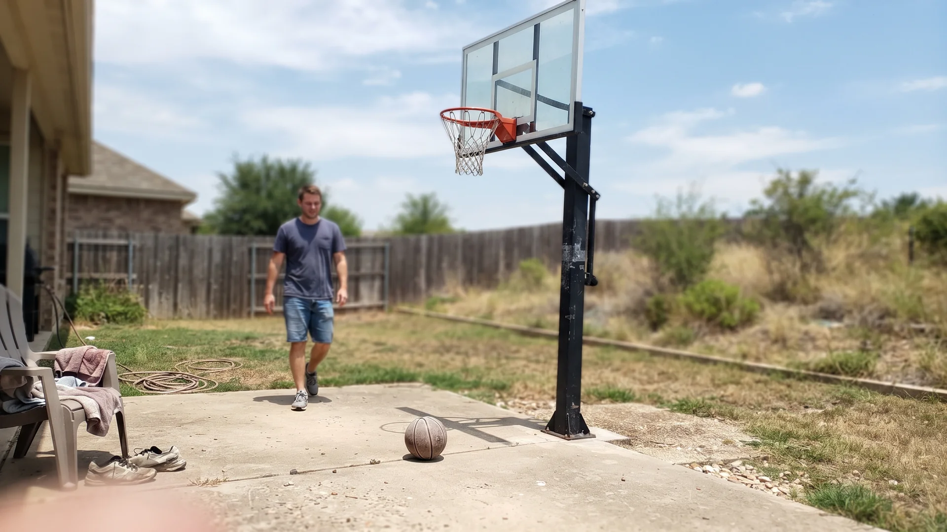 In-ground basketball goal with tempered-glass backboard beside a backyard court