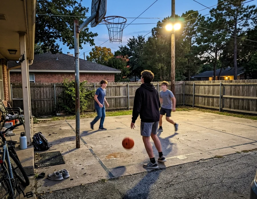 Teenagers playing on a lit backyard basketball court at dusk